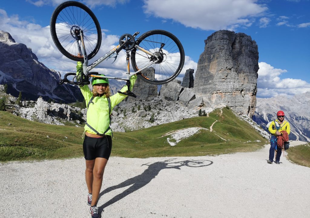 Cyklotúry v Dolomitoch: Tamara s bicyklom nad hlavou pred skalami Cinque Torri